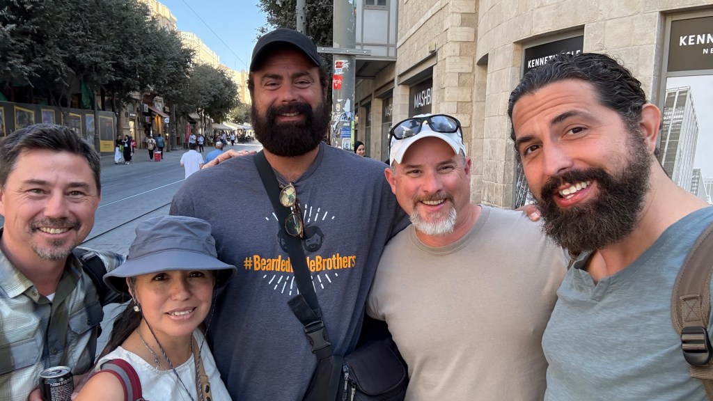 A group of five people posing for a photo on a street, with shops and trees in the background.